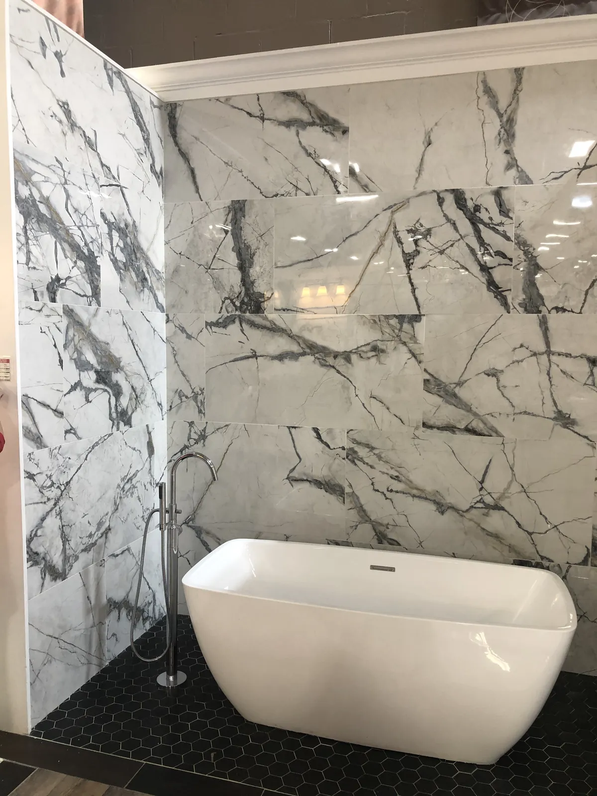 Freestanding Soaking Tub — A sculptural freestanding tub against bookmatched marble, finished with crown molding and a black hexagon mosaic floor.
