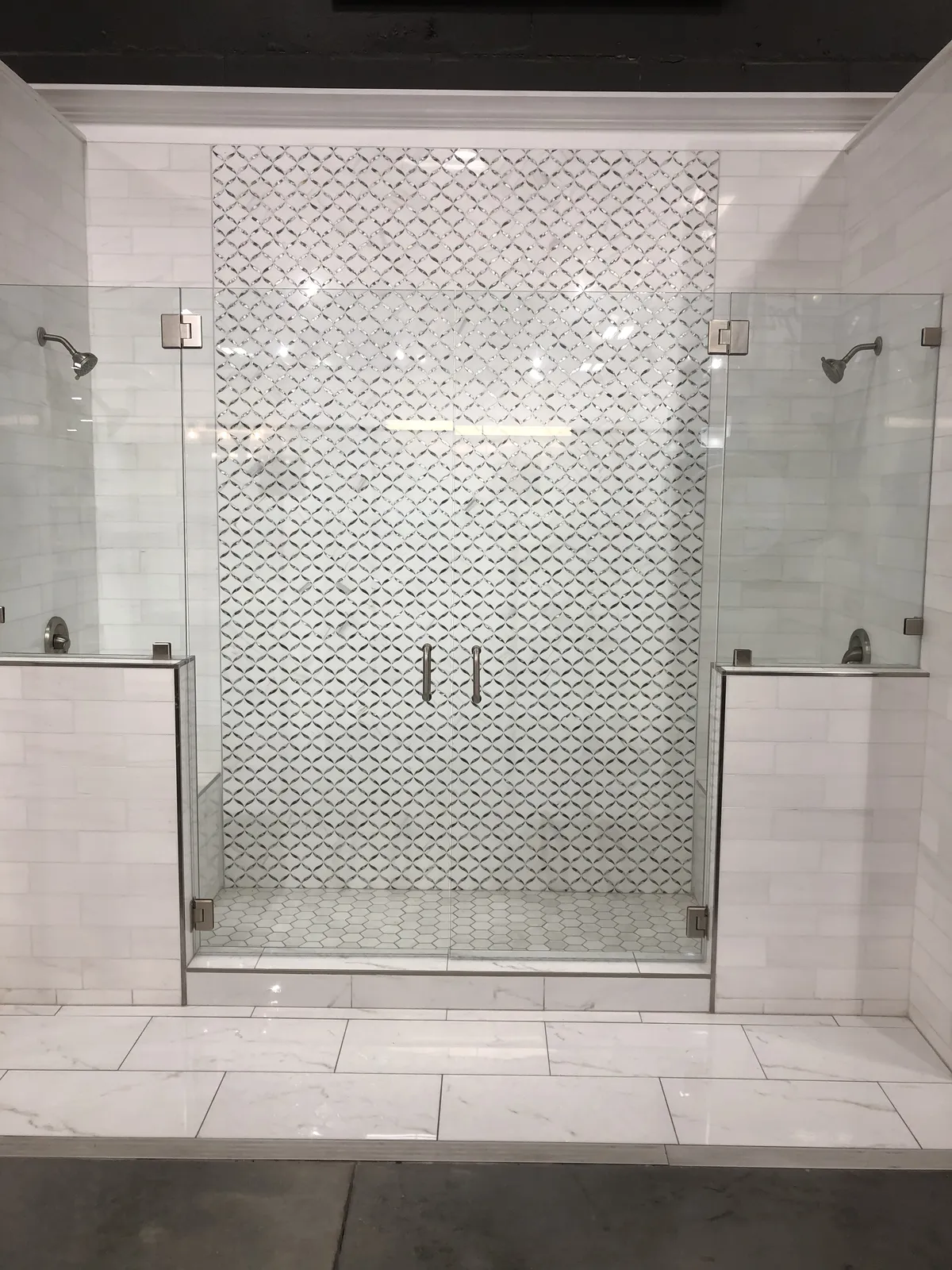Frameless Double Shower — Dual rainfall showers behind frameless glass, anchored by a hand-set lattice mosaic feature wall.